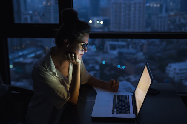 La mujer está trabajando con la computadora portátil en casa durante la noche.