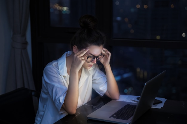 La mujer está trabajando con la computadora portátil en casa durante la noche.