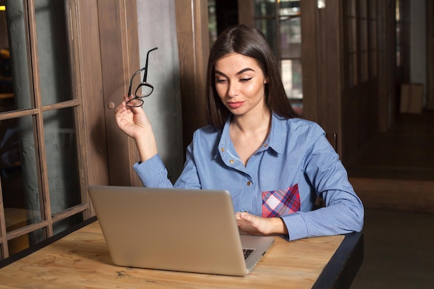 La mujer está trabajando con una computadora portátil gris y gafas en la mano