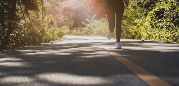 Una mujer está trotando en la carretera de un parque, ella está corriendo en un parque donde mucha gente viene para trotar por la mañana y por la noche, correr es una actividad popular. Concepto de salud con jogging.