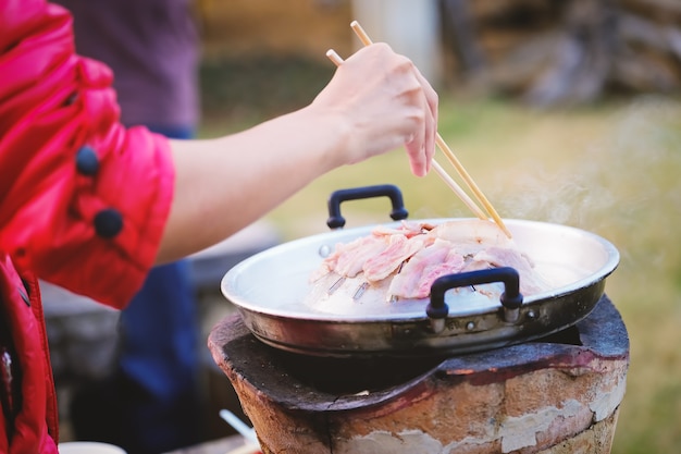 La mujer está usando palillos para sujetar la carne de cerdo en la sartén