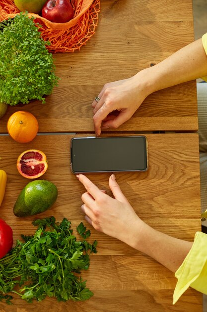 La mujer está usando tableta digital o smarthone, buscando receta de cocina en la cocina en casa, concepto de comida saludable, vegana o dieta. Compras en línea de comestibles