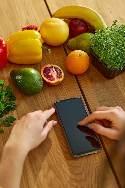 La mujer está usando tableta digital o smarthone, buscando receta de cocina en la cocina en casa, concepto de comida saludable, vegana o dieta. Compras en línea de comestibles