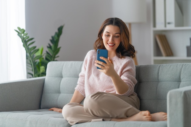 La mujer está usando un teléfono sentado en un sofá