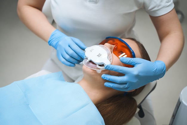 La mujer está visitando al dentista y acostada en gafas protectoras en una silla mientras es tratada con una máquina moderna especial