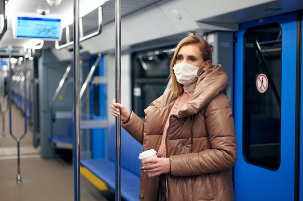 Mujer en la estación de metro con máscara protectora de higiene quirúrgica en la cara evita el riesgo de coronavirus