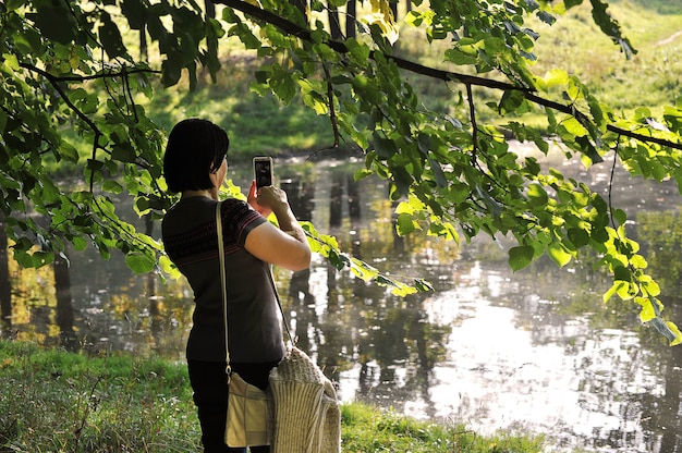 Mujer en el estanque toma una foto del paisaje en su teléfono