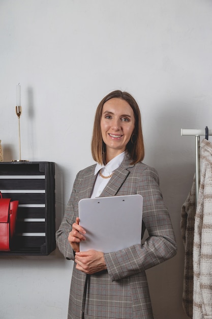 Mujer estilista milenaria con tableta junto a la ropa en la elegante barandilla en el vestidor