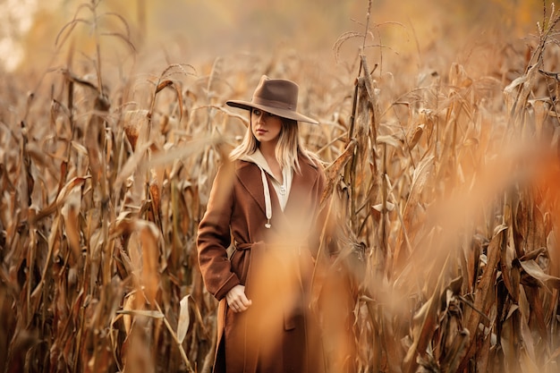 Mujer de estilo en abrigo y sombrero en campo de maíz en temporada de otoño