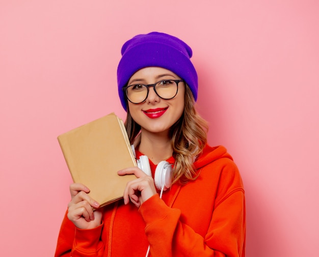 Mujer de estilo con auriculares y libros en pared rosa