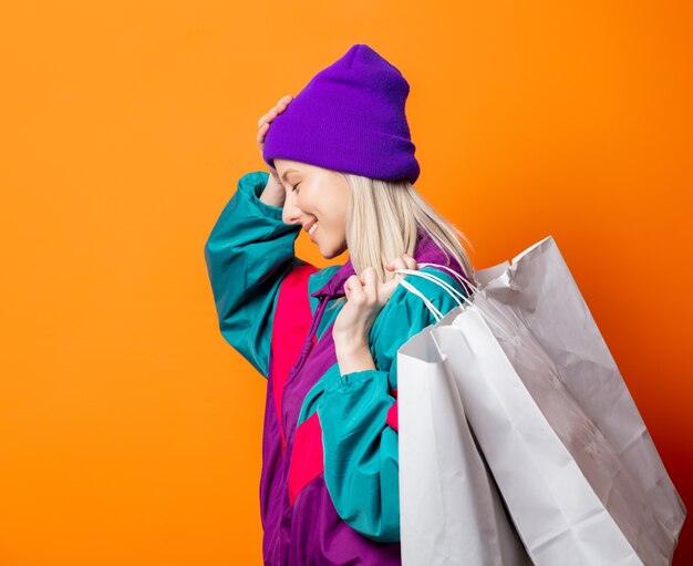 Mujer de estilo en chándal de los años 90 con bolsas de la compra en naranja