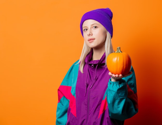 Mujer de estilo en chándal de los años 90 con calabaza en naranja