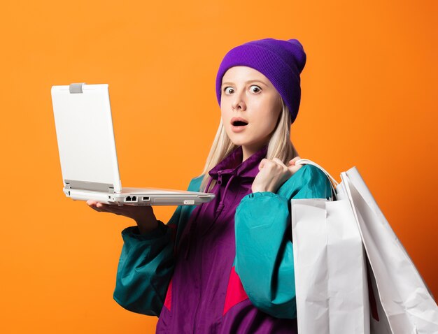 Mujer de estilo en chándal de los años 90 con cuaderno y bolsas de compras en naranja