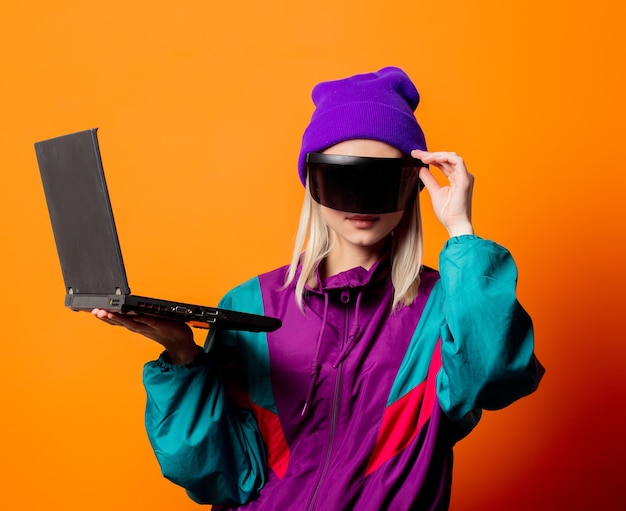 Mujer de estilo en chándal de los años 90 y gafas de realidad virtual con cuaderno en naranja