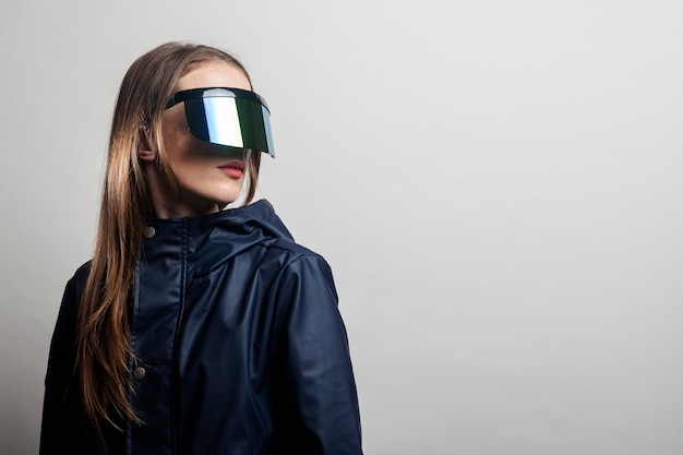 Mujer de estilo con gafas de realidad virtual y una chaqueta azul sobre un fondo claro.