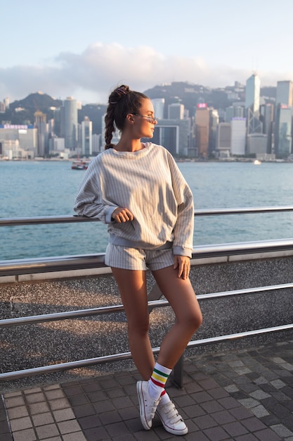 Mujer con estilo joven está posando en el puerto de Victoria, la ciudad de Hong Kong.