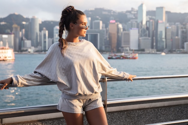Mujer con estilo joven está posando en el puerto de Victoria, la ciudad de Hong Kong.