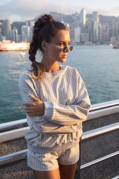 Mujer con estilo joven está posando en el puerto de Victoria, la ciudad de Hong Kong.