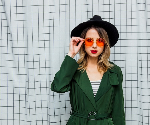 Mujer de estilo joven en gafas de sol y manto verde en estilo años 90