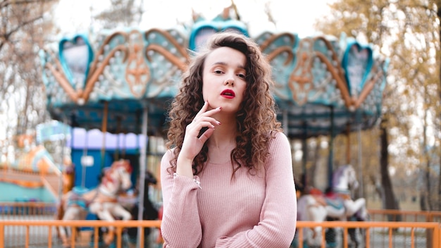 Mujer con estilo joven inconformista posando al aire libre en el parque con carruseles