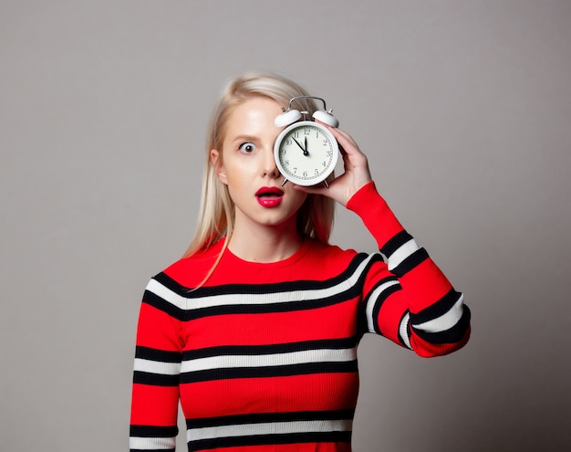 Mujer de estilo en suéter rojo con reloj despertador en pared gris