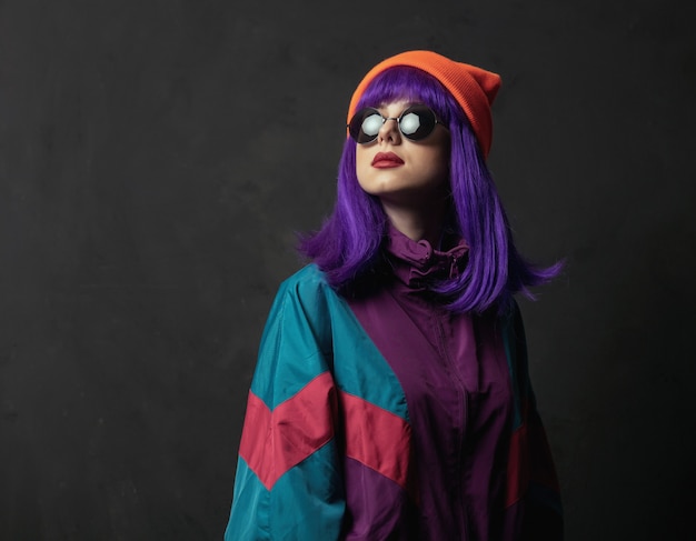 Mujer de estilo en traje deportivo y gafas de sol en la pared oscura