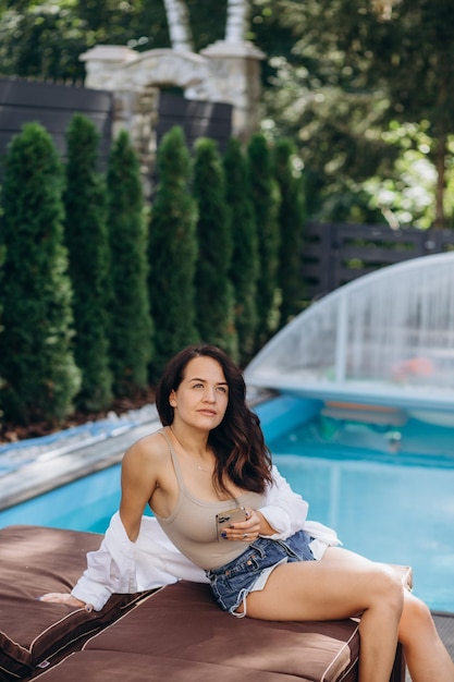 Foto mujer de estilo de vida de día de verano relajarse y relajarse cerca de la piscina de lujo tomar el sol en el resort de playa al aire libre del hotel concepto de vacaciones y verano