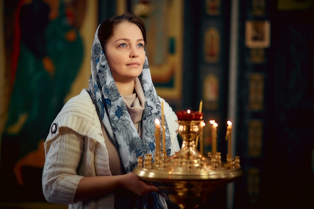 Mujer de estilo de vida enciende velas en la Iglesia, rezando frente al icono