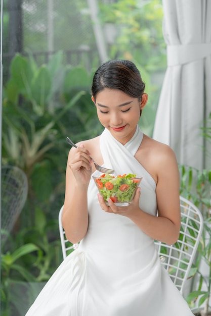 Mujer de estilo de vida saludable comiendo ensalada sonriendo feliz en el interior en un hermoso día