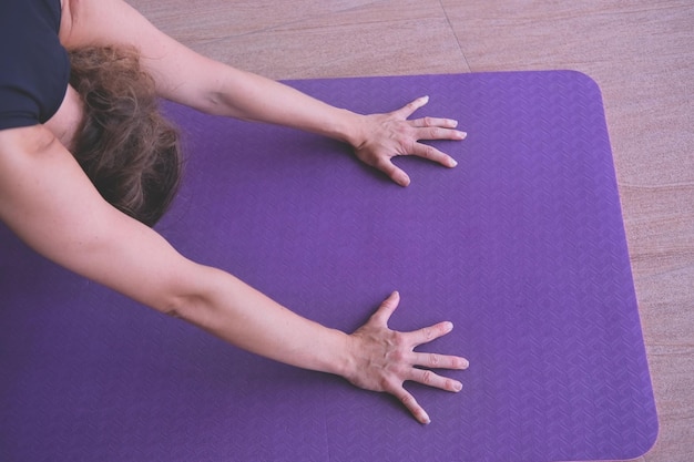 Una mujer se estira sobre una colchoneta de yoga con las manos sobre la alfombra