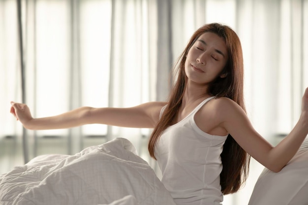 Mujer estirándose en la cama después de despertarse por la mañana en el fondo de una gran ventana en el dormitorio