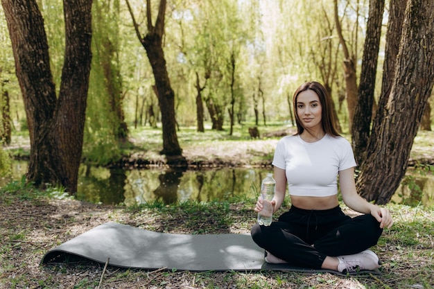 Mujer estirándose en una estera de yoga en el bosque Concepto de estilo de vida saludable Mujer toca sus pies Sesión de yoga natural en hermosos bosques entre pinos Mujer delgada con sujetador negro, leggins y calcetines