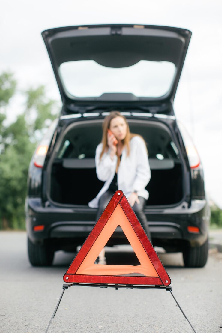 Mujer estresada mirando un auto roto y revisando el motor en la carretera rural a la vista lateral