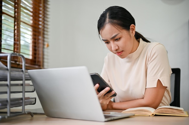 Mujer estresante joven que trabaja desde casa con teléfono inteligente y computadora portátil