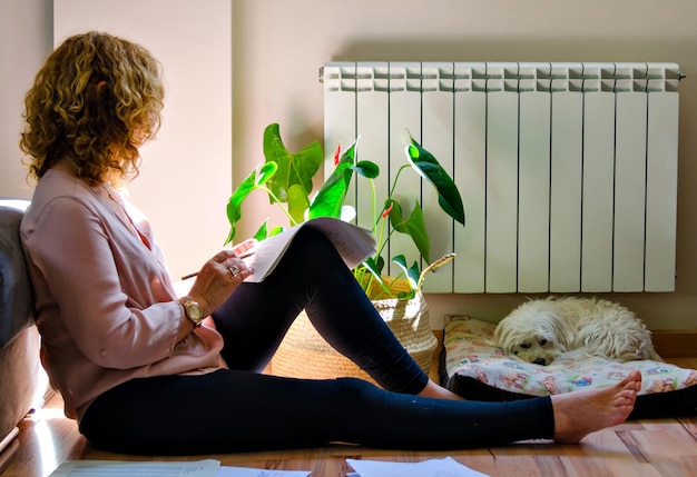 Mujer estudiando en casa, recostada en el sofá de casa junto a la ventana