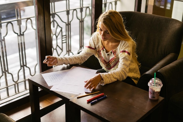 Mujer estudiando escribir en papel mientras está sentada en un lugar interior