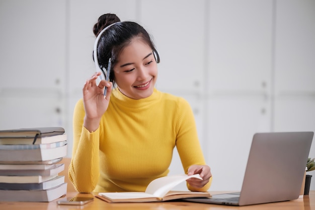 Mujer estudiante asiática joven adulta tomando notas mientras usa una computadora portátil en casa Mujer asiática aprendiendo en línea escuchando videoconferencia virtual Concepto de negocios y educación