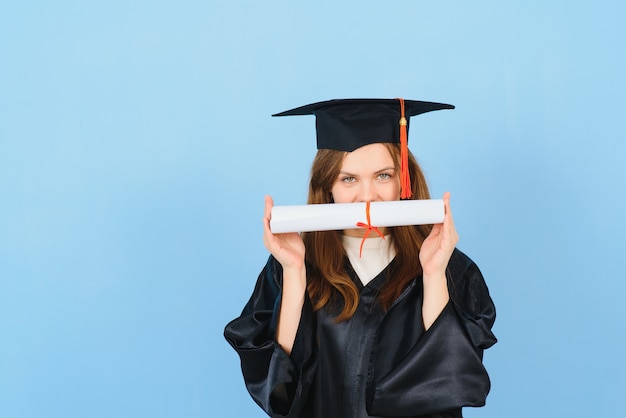 Mujer estudiante graduada vistiendo toga y sombrero de graduación, sobre fondo azul.