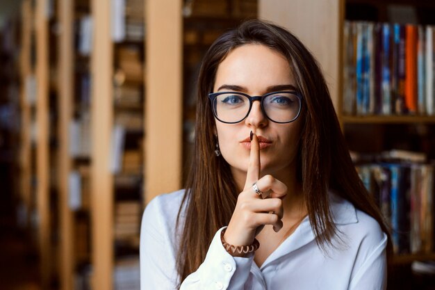 Mujer estudiante haciendo gesto de silencio en una biblioteca