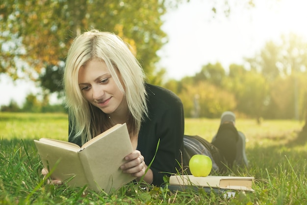 Foto mujer estudiante leyendo sobre hierba con manzana