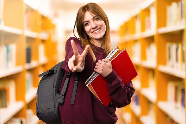 Mujer del estudiante que hace gesto de la victoria en fondo desenfocado. De vuelta a la escuela