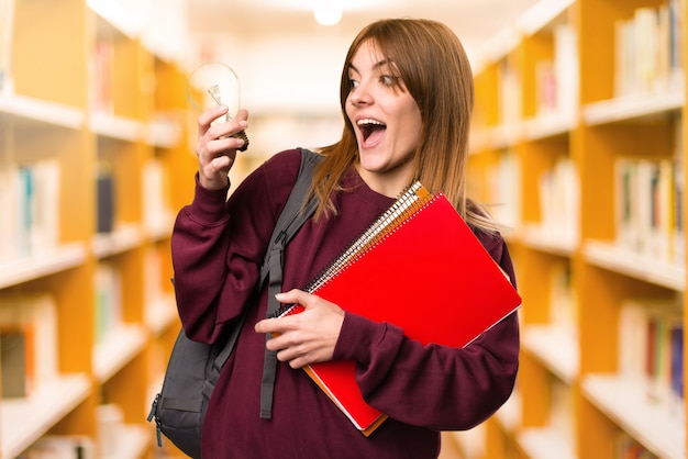 Mujer del estudiante que sostiene un bulbo en fondo desenfocado. De vuelta a la escuela