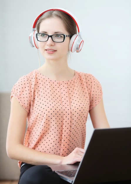 La mujer estudiante se sienta con una computadora portátil en su regazo, escuchando música y aprendiendo.