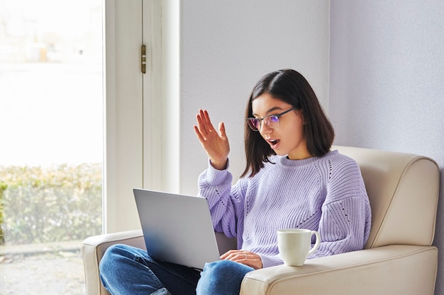 Mujer de etnia joven sorprendida con gafas mirando en la computadora