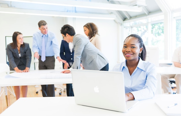 Mujer étnica africana sonriendo a la cámara mientras trabaja en su computadora portátil con reunión de negocios como el