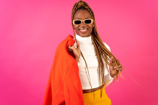 Mujer étnica negra con trenzas sobre un fondo rosa posó a la moda con un traje rojo y una camiseta blanca