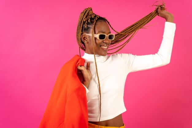 Mujer étnica negra con trenzas sobre un fondo rosa posó a la moda con un traje rojo y una camiseta blanca