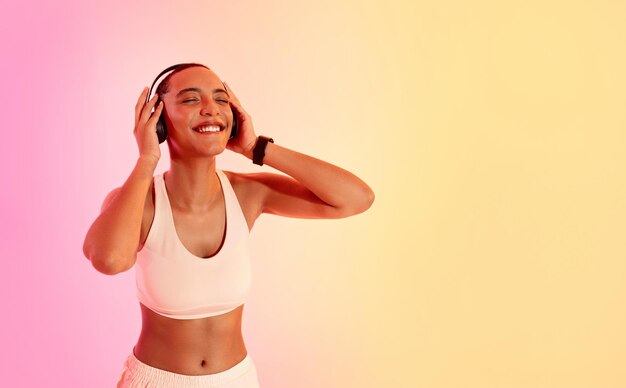 Mujer eufórica con un corte de buzz disfrutando de la música en auriculares con un sujetador deportivo blanco