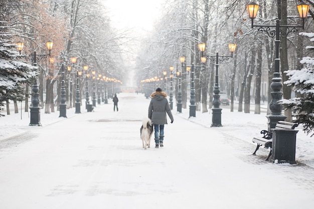 Mujer europea caminando con el perro malamute de Alaska en la ciudad de invierno por la noche