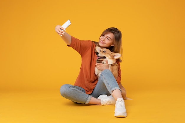 Mujer europea emocionada tomando una selfie con su bonito perro corgi mirando a la cámara del teléfono y abrazándose